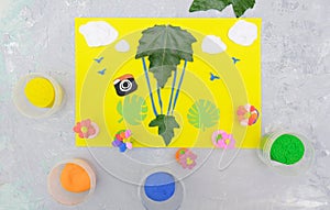Child making card from paper, plasticine and natural leaves. Air balloon, clouds, birds, flowers... Inspiration for children.