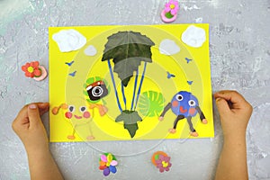 Child making card from paper, plasticine and natural leaves. Air balloon, clouds, birds, flowers... Inspiration for children.