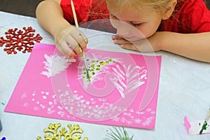 Child making a greeting card. Craft for children. Nice greeting card with a Christmas snowy forest. . Top view