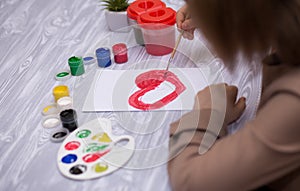 Child making homemade greeting card. Little girl paints heart on homemade greeting card as gift for Mother Day.