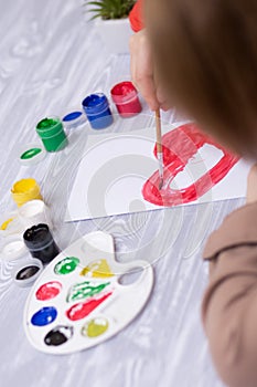 Child making homemade greeting card. Little girl paints heart on homemade greeting card as gift for Mother Day.