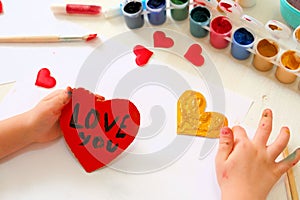 Child making homemade greeting card. A little girl paints a hearts as a gift for Motherâ€™s Day or VAlentines day. Traditional