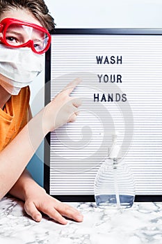 Child in mask pointing at Sanitizer, soap and wash your hands sign