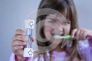 Child measures time while brushes her teeth. Healthy habits, dentalcare concept. Close up photo