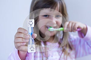 Girl kid measures time while brushes her teeth. Healthy habits, dentalcare concept. Close up photo