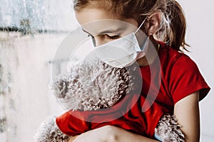 child in a medical mask sits on a window with a bear. graft