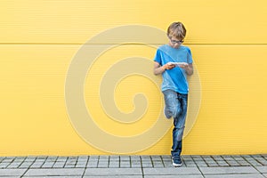 Child with mobile phone standing near yellow wall outside