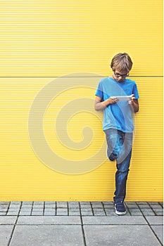 Child with mobile phone standing near yellow wall outside