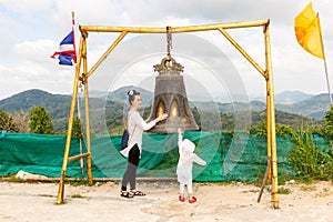 Child and mom near Thai gong in Phuket. Tradition asian bell in Buddhism temple in Thailand. Famous Big bell wish near Gold Buddha