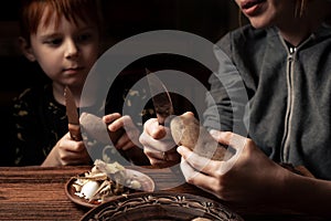 Child with mom peels potatoes on a dark background. A woman teaches her son to peel potatoes