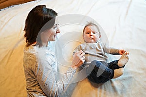 Child and mother on bed. Mom and baby boy playing in sunny bedroom. Parent and little kid relaxing at home. Family having fun