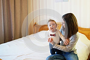 Child and mother on bed. Mom and baby boy playing in sunny bedroom. Parent and little kid relaxing at home. Family having fun