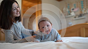 Child and mother on bed. Mom and baby boy playing in sunny bedroom. Parent and little kid relaxing at home. Family having fun