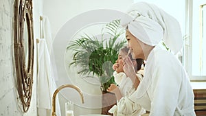 Child and mother brushing teeth, look at mirror in modern white bathroom Spbd. Asian parent