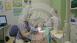 Child with a mother at a dentist`s reception. The girl lies in the chair, behind her mother. The doctor works with an