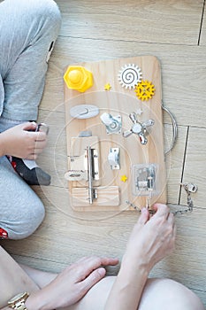 Child and mother are playing with busy board toy on the wooden floor together. Childrenâ€™s educational busy board toy for