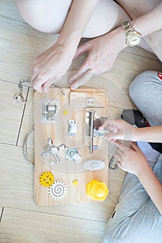 Child and mother are playing with busy board toy on the wooden floor together. Childrenâ€™s educational busy board toy for