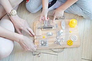 Child and mother are playing with busy board toy on the wooden floor together. Childrenâ€™s educational busy board toy for