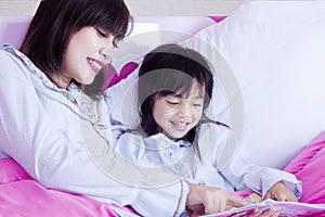 Child and mother read book on bed