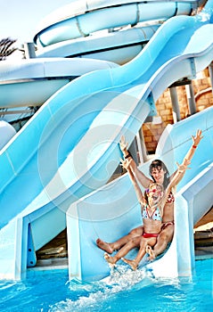 Child with mother on water slide at aquapark.