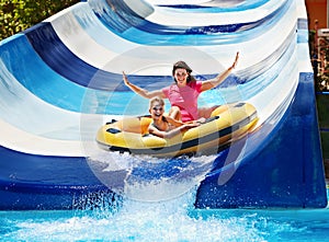 Child with mother on water slide at aquapark.