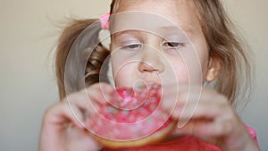 Child mouth bites rose donut. Closeup baby girl eating doughnut with glase. Delicious, sweet, sweettooth.