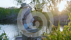 Child in nature, cute beautiful baby in hat and stick in hands has fun on pier playing in pond