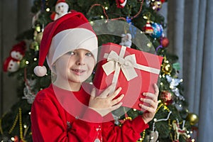 Child near Christmas tree with gift box. Cute little boy is standing near Christmas tree with gift. Merry Christmas and Happy New