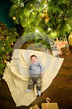 Child near christmas tree top view. Closeup portrait of smiling cute little child in holiday christmas interior near festive tree