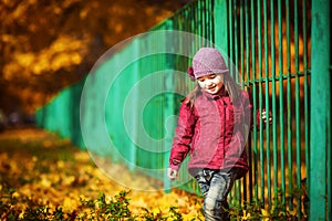 Child near the green fence on the background of autumn