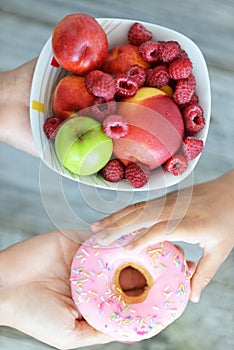 Child not resisting the temptation to choose an attractive but unhealthy doughnut instead of a healthy bowl of fresh fruits photo