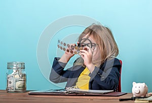 Child numismatist with metal coin in a transparent plastic protection square capsule. Kid with a magnifying glass is