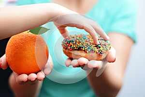 Child obesity concept with little girl hand choosing a sweet and unhealthy doughnut instead of a fruit