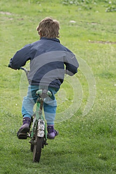 A child in old clothes rides a bicycle. Back view