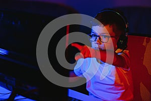 Child online broadcasts computer game, boy streams in headphones on rgb lighting background