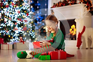 Child opening present at Christmas tree at home. Kid in elf costume with Xmas gifts and toys. Little girl with gift box and candy