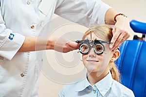 Child optometry concept. Young girl with phoropter during sight testing