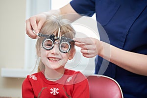 Child optometry concept. Young girl with phoropter during sight testing. BeH3althy