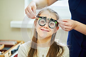 Child optometry concept. Young girl with phoropter during sight testing. BeH3althy