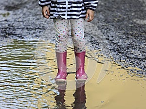 Child outdoor jump into puddle in boot after rain