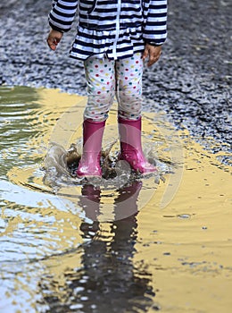 Child outdoor jump into puddle in boot after rain