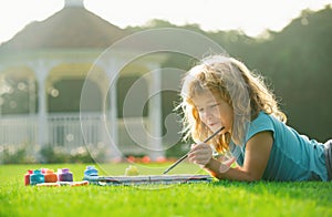 Child painting drawing art. Kid draws in park laying in grass having fun on nature background. Painting school lesson