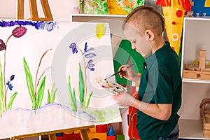 Child painting finger on easel. Kid boy learn paint school.