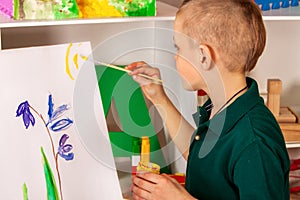 Child painting finger on easel. Kid boy learn paint school.