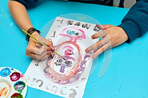 Child painting with watercolors, drawing a face, no faces are shown, only hands