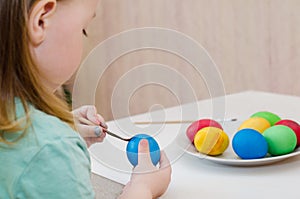 The child paints blue easter egg by brush