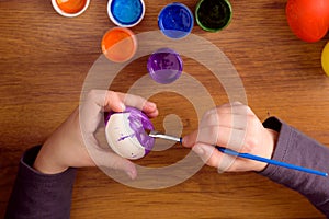 The child paints an egg for Easter. Set of paints on wooden background