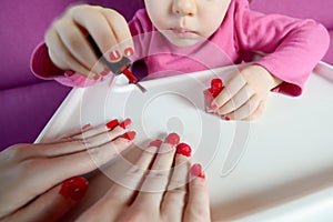 The child paints the nails of his mother with varnish