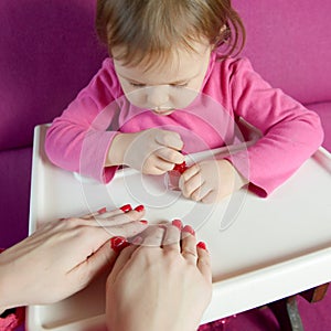 The child paints the nails of his mother with varnish