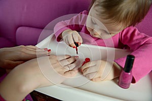 The child paints the nails of his mother with varnish